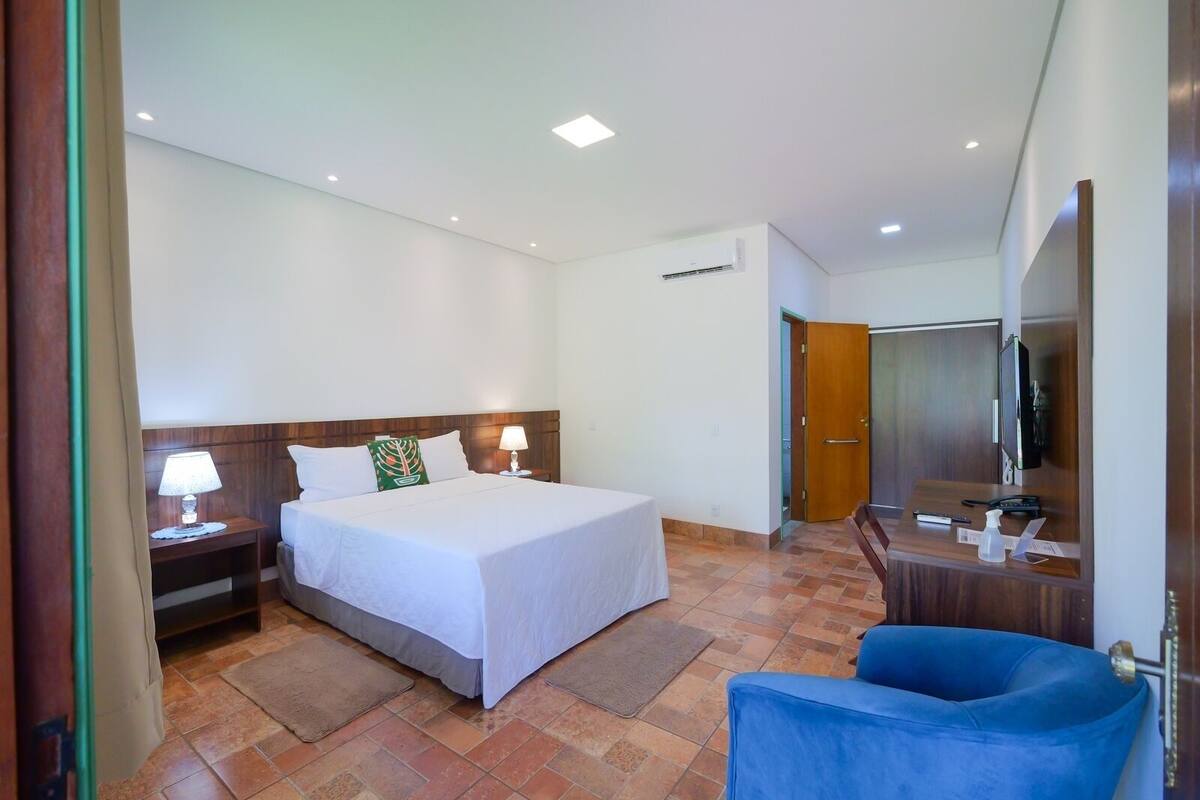 A hotel room with a bed, bedside tables, a chair, a TV, and a door.