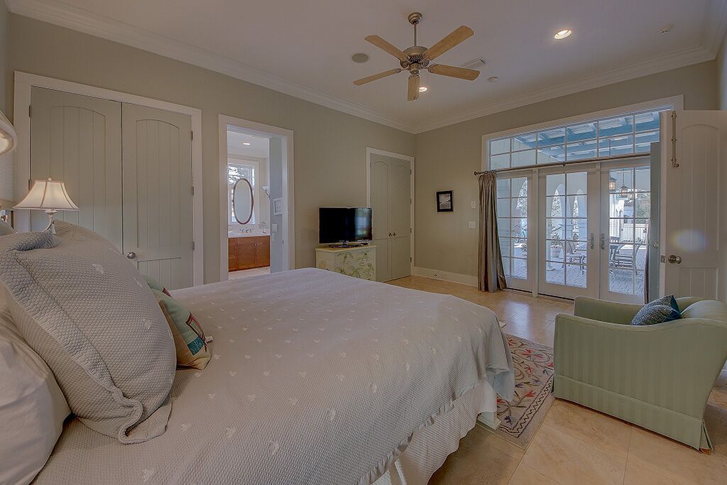 A bedroom with a large bed, a ceiling fan, a television, and a view through a glass door.