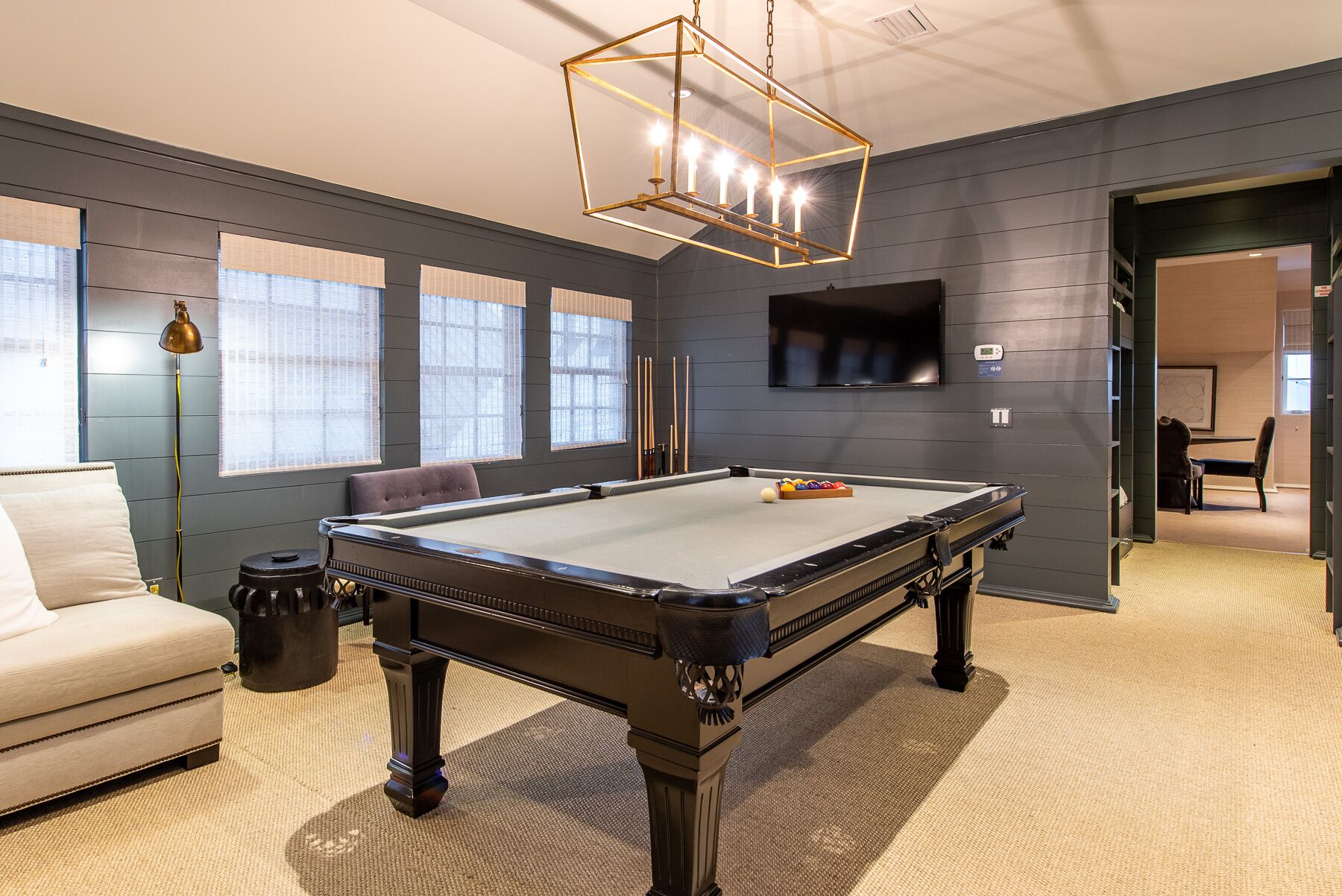 A pool table in a room with a sofa, a lamp, and a television on the wall.