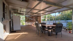 Une terrasse couverte avec une table et des chaises, un réfrigérateur et une vue sur l’extérieur.