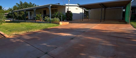 A residential property with a covered driveway, a garage, and a lawn with small shrubs.