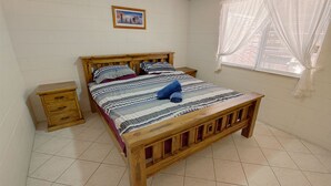 A wooden bed with a striped bedspread, a wooden nightstand, and a window with sheer curtains.