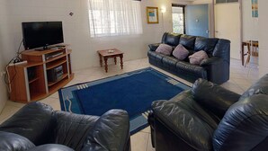 A living room with a leather sofa, a television on a wooden stand, a small wooden table, and a blue rug.