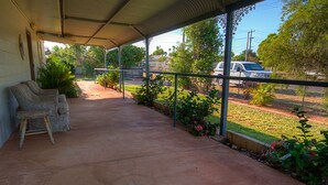 A covered patio area with a concrete floor, outdoor furniture, and a view of a street with parked cars and greenery.