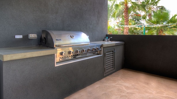 A modern outdoor kitchen with a stainless steel grill, a sink, and a ventilation hood.