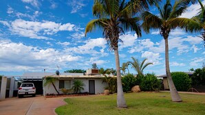 A single-story house with a driveway, a parked car, and palm trees.