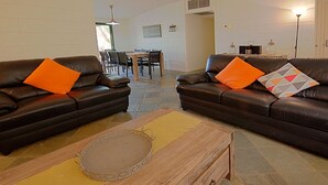 A living room with two dark leather sofas, each with an orange pillow, a wooden coffee table, and a patterned rug.