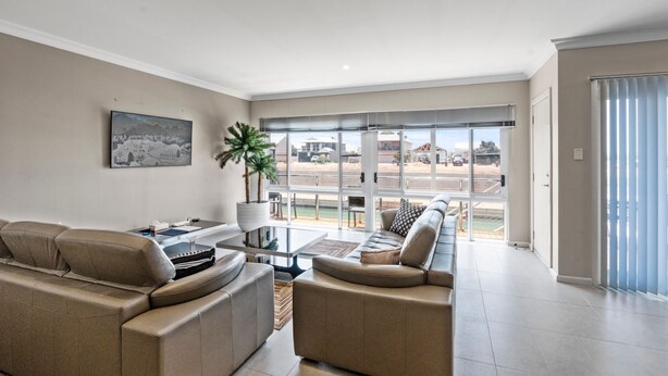 A spacious living room with a large window, a sofa, a coffee table, and a potted plant.