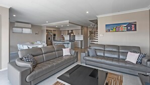 A modern living room with two grey sofas, a coffee table, and a dining area with a white table and chairs.