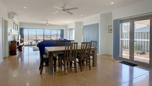 Un'ampia sala da pranzo con un grande tavolo e sedie, una ventola a soffitto e vista all'esterno attraverso una porta in vetro.