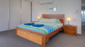 Un letto di legno con una coperta a righe e due asciugamani blu, un comodino con una lampada e un piccolo tavolino di legno.