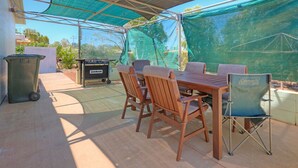 An outdoor patio with a wooden table and chairs, a Coleman folding chair, a Jumbuck grill, and a trash can. - Blue Moon - Family friendly, comfy home. (Exmouth)