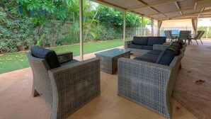 Een terras buiten met wicker meubels, een klein tafeltje en uitzicht op een verzorgd gazon en bomen.