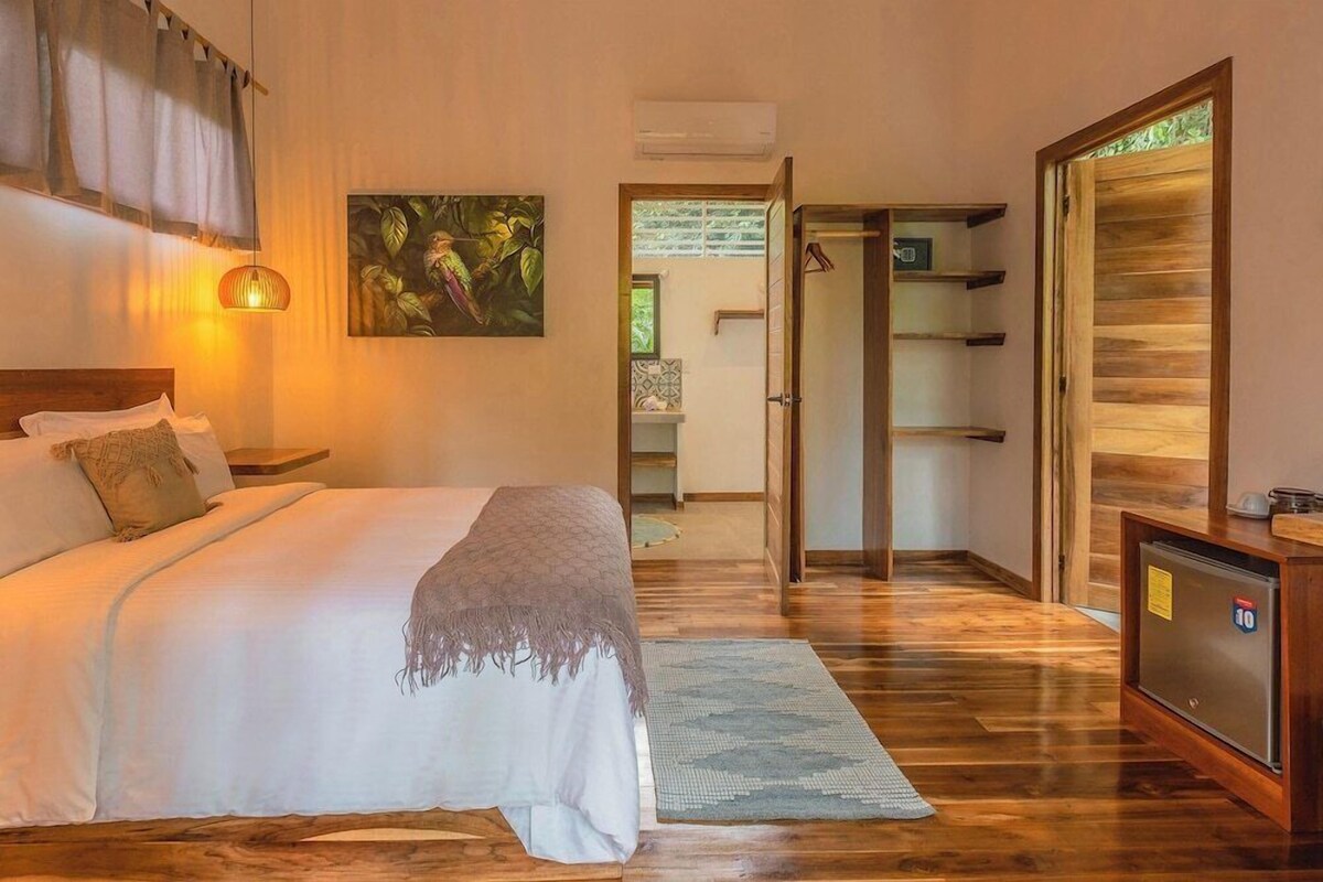 A bedroom with a bed, bedside table, hanging light, and a painting.