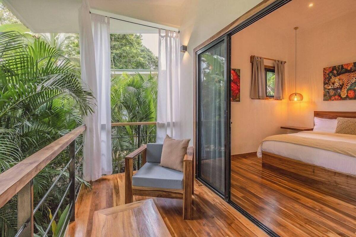 A balcony with a wooden chair, a table, and a bed with a headboard.