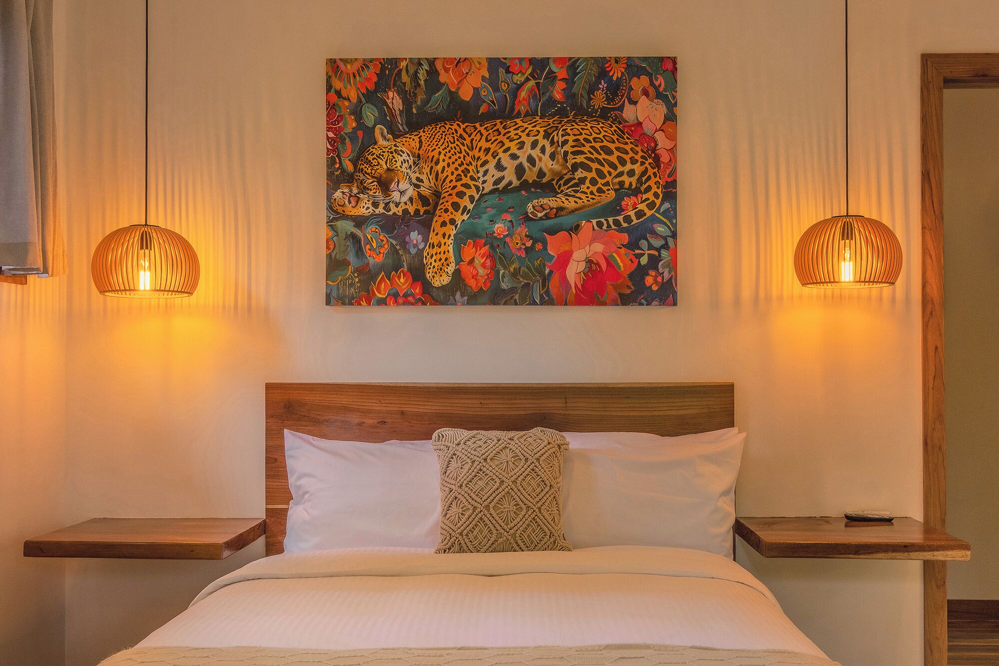 A bedroom with a bed, a headboard, two bedside tables, a wall-mounted painting of a leopard, and two hanging lamps.