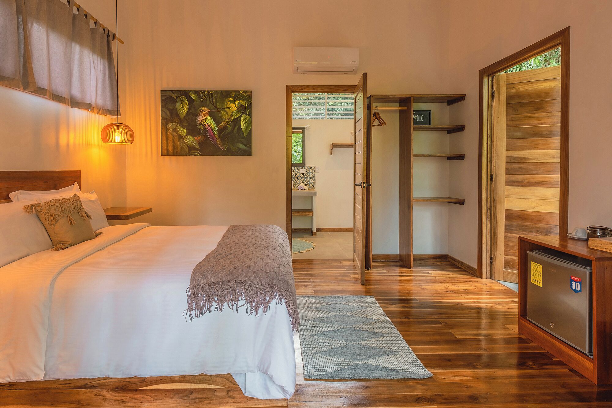 Een slaapkamer met een bed, nachtkastje, lamp en een schilderij van een vogel.