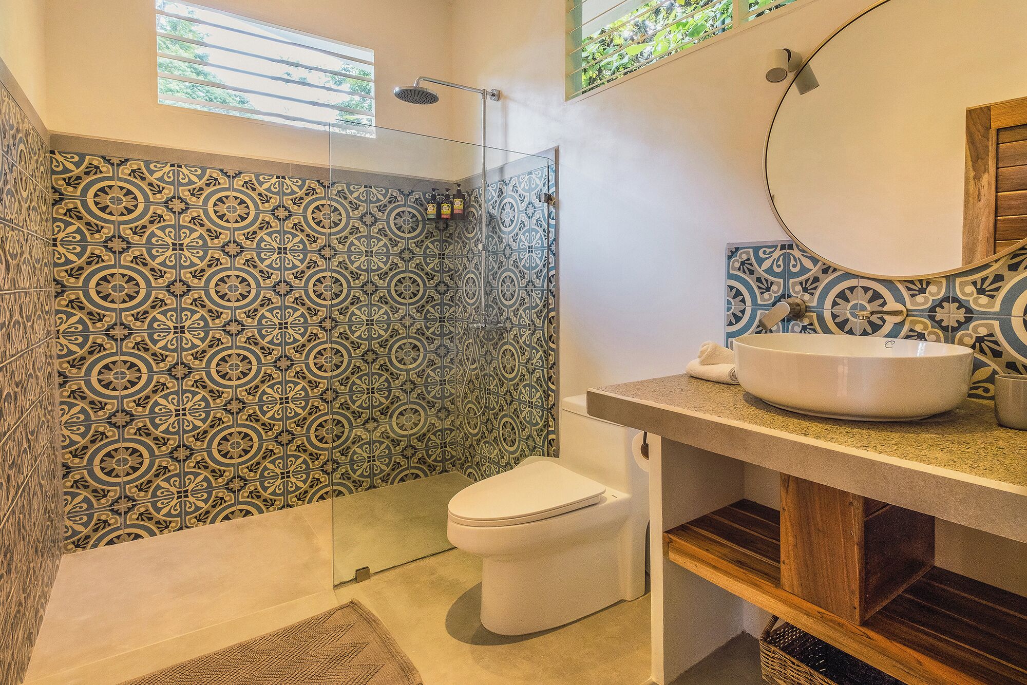 A bathroom with patterned tiles, a white toilet, a glass-enclosed shower, and a sink with a mirror.