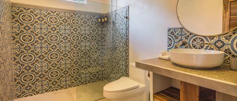 A bathroom with patterned tiles, a white toilet, a glass-enclosed shower, and a sink with a mirror.