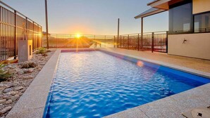 En pool med udsigt til solnedgang, omgivet af et hegn og en bygning.
