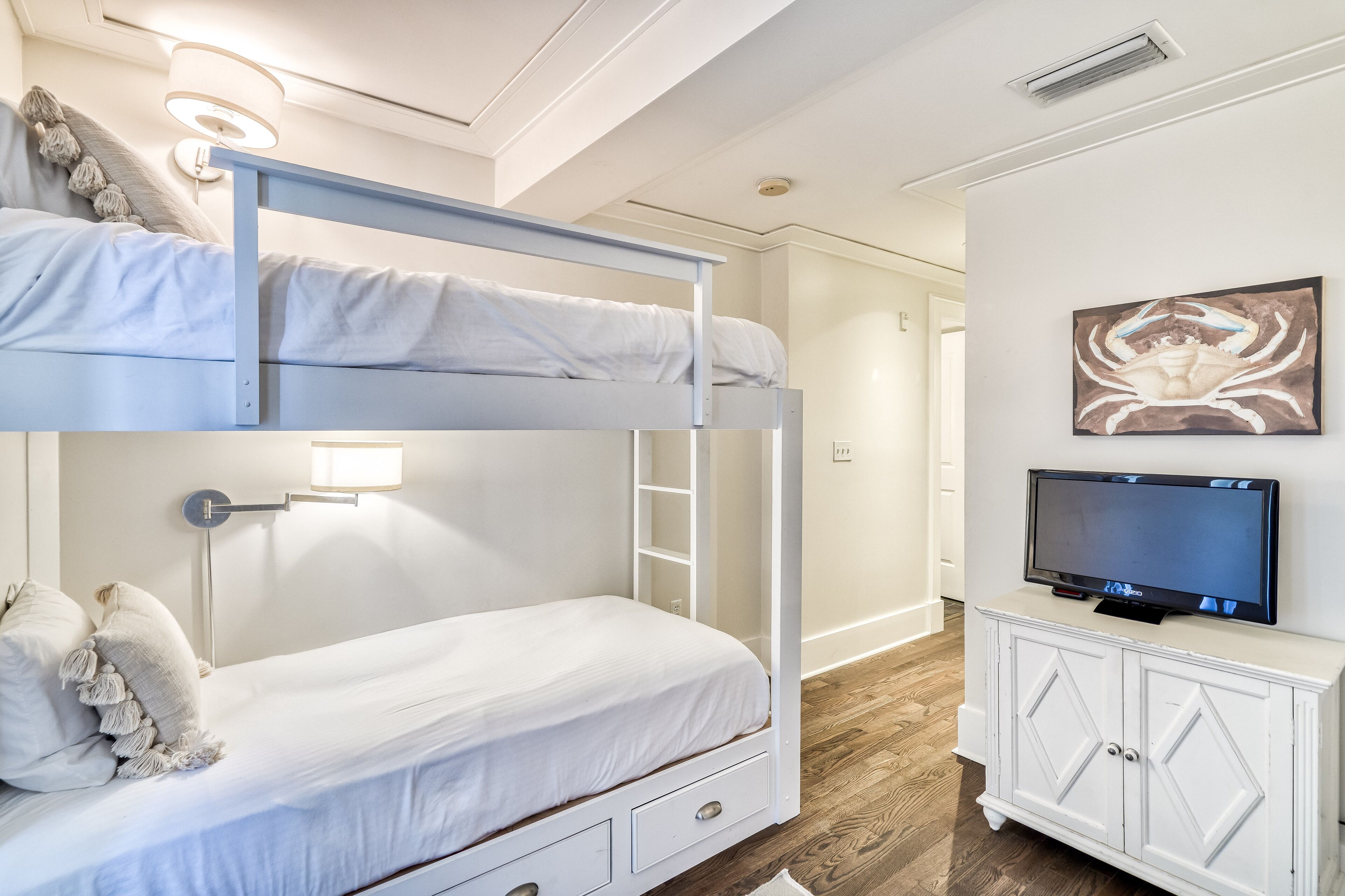 Una cama litera con una escalera, un televisor sobre un mueble y un cuadro en la pared.