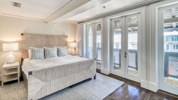 Une chambre dotée d’un grand lit, de deux tables de chevet avec des lampes, d’une tête de lit à motifs et donnant sur un paysage grâce à de grandes portes-fenêtres coulissantes.