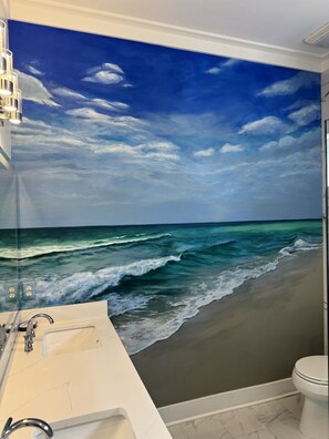 Ein Badezimmer mit einer großen Wandmalerei einer Strandansicht, einem weißen Waschbecken und einer Toilette.