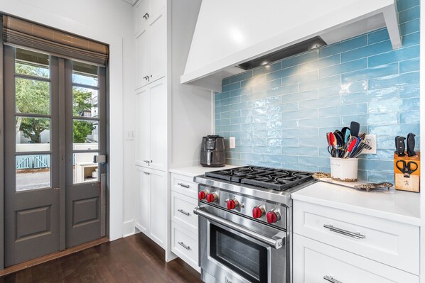 A modern kitchen with white cabinets, a stainless steel stove, and a blue-tiled backsplash.