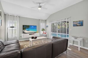 A modern living room with a flat-screen TV, leather sofa, and a view of a pool.