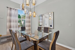 A dining area with a glass table surrounded by chairs, a chandelier, and a large mirror on the wall.