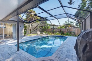 A covered outdoor swimming pool with a view of the backyard, including a wooden fence and plants.