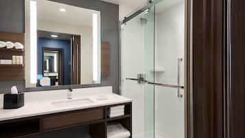 A modern bathroom with a large mirror, a white sink, a glass shower enclosure, and neatly folded towels.