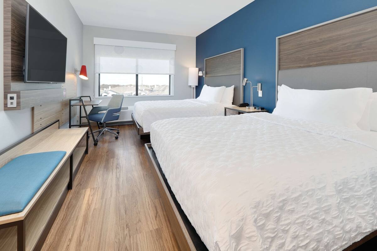 Habitación de hotel con dos camas, un escritorio, una silla, un televisor montado en la pared y una ventana con vistas.