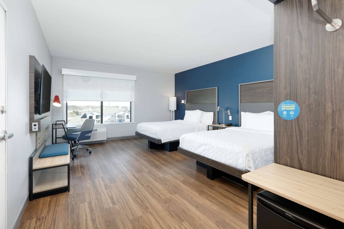 Habitación de hotel con dos camas, un escritorio, una silla, un televisor y una ventana con vista a la ciudad.