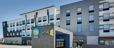 A modern hotel building with a sign reading "tru HOME 2 by Hilton".
