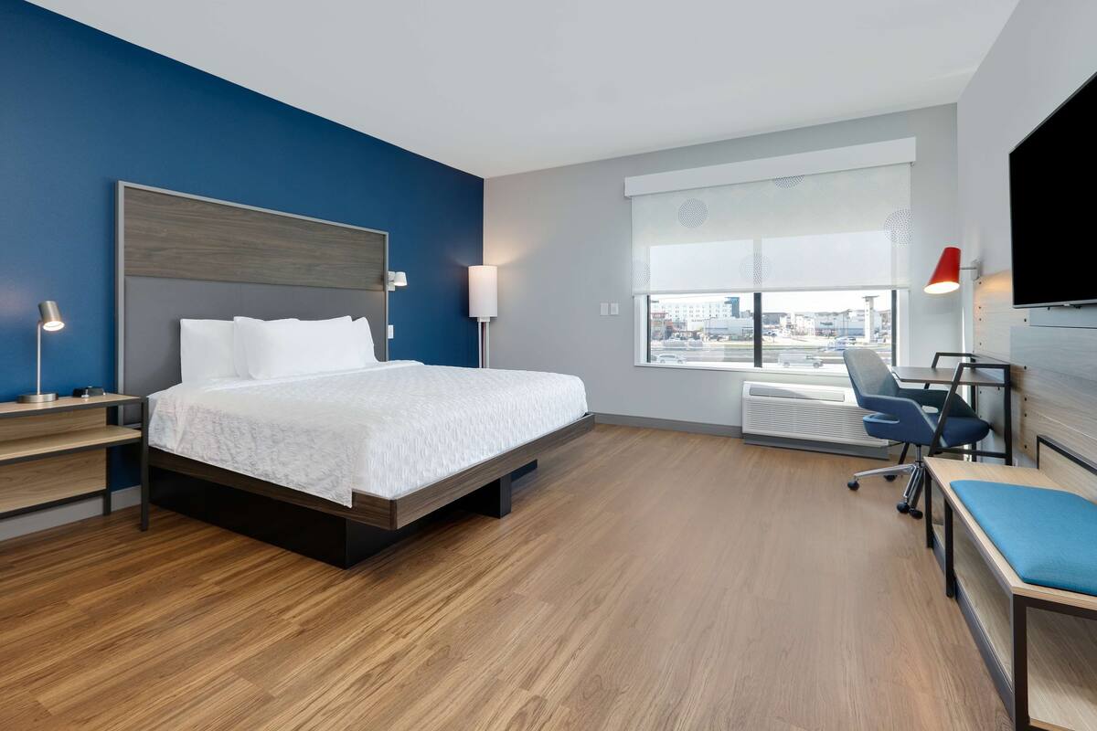 Habitación de hotel moderna con una cama grande, un escritorio y una silla. Hay una ventana con vistas a la ciudad.