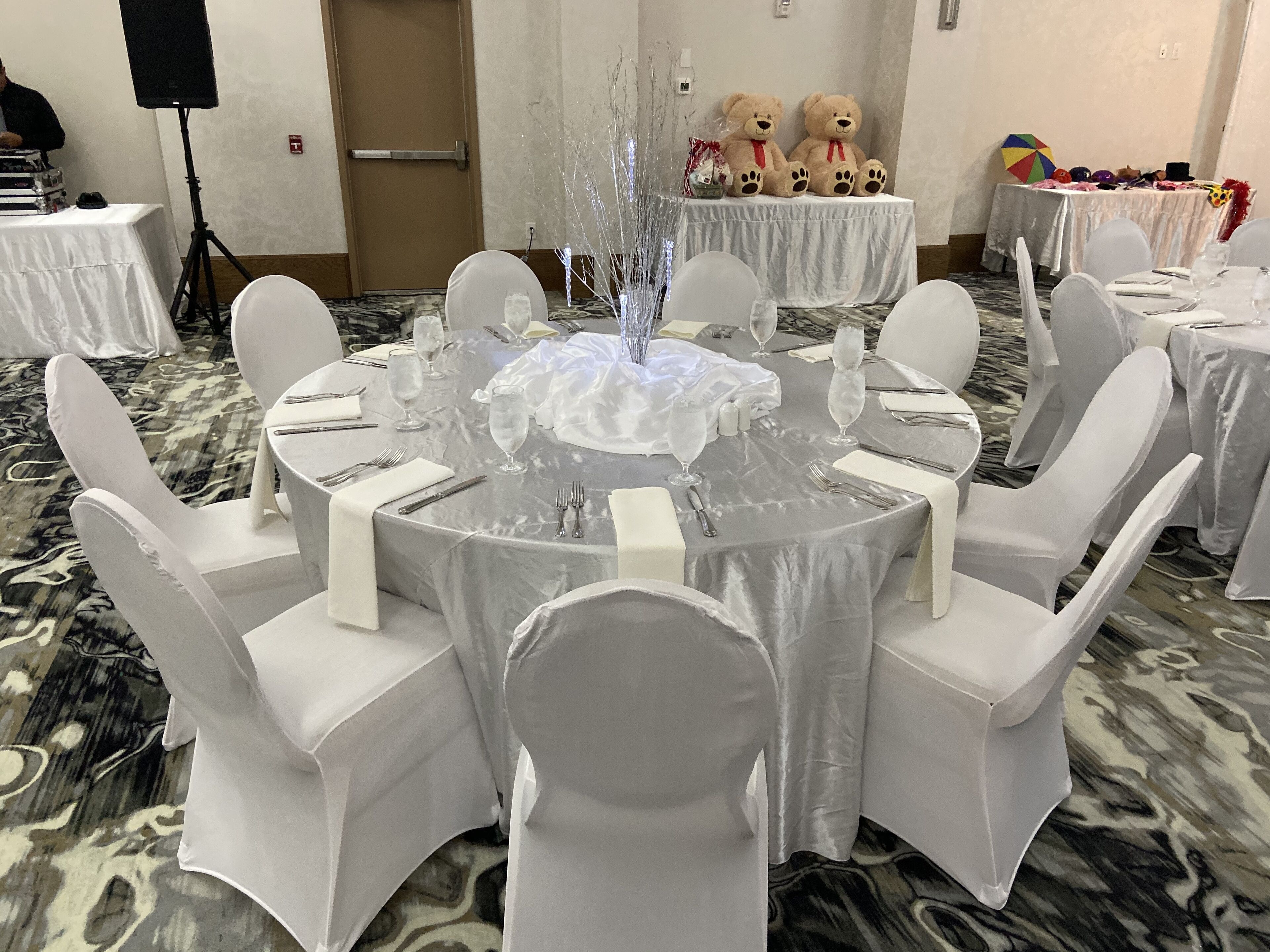 A round table with a clear water feature in the center, surrounded by white chairs and covered with a white tablecloth.