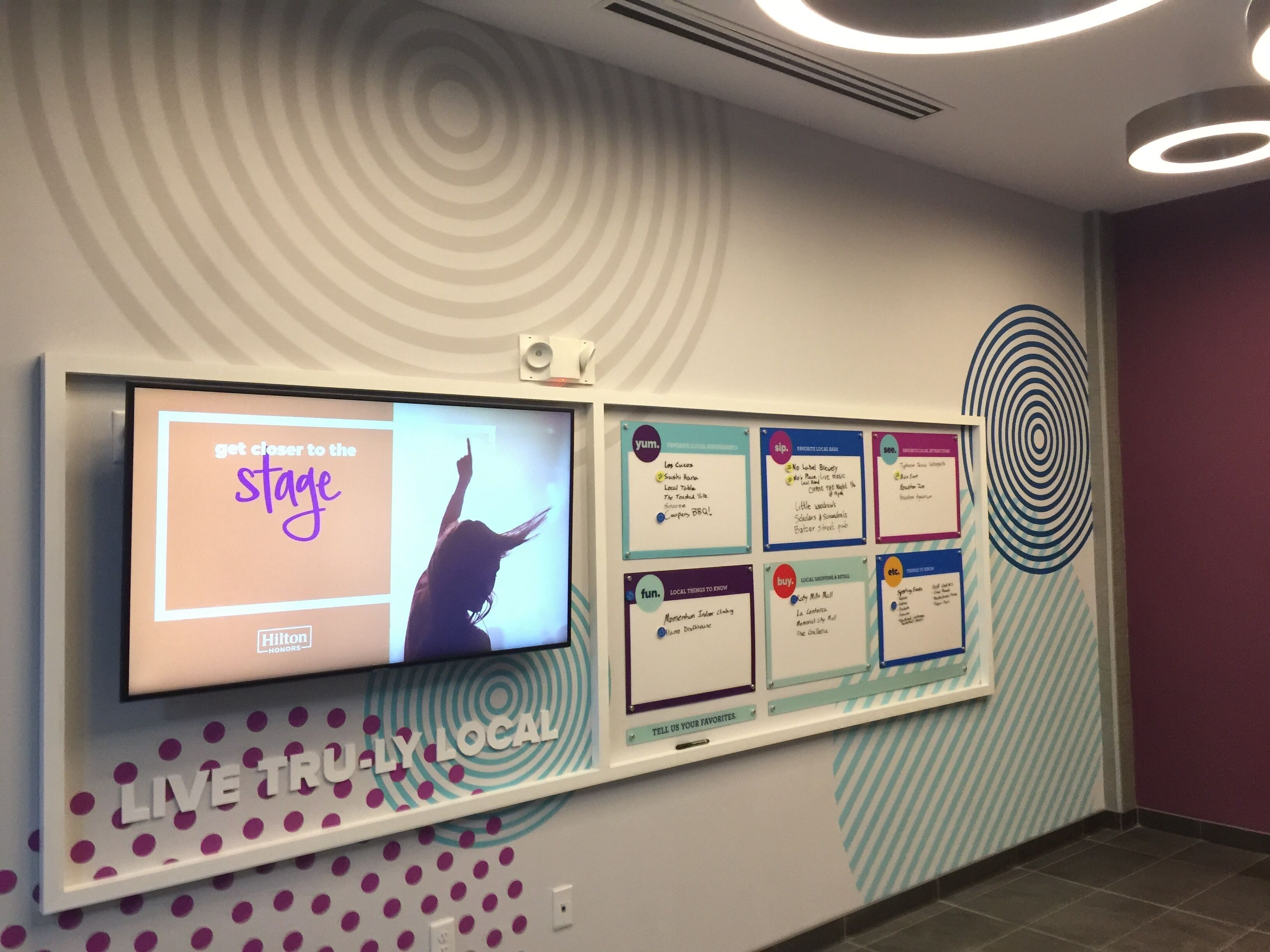 A wall with a TV screen displaying 'get closer to the stage' and a 'LIVE TRU-LY LOCAL' sign.