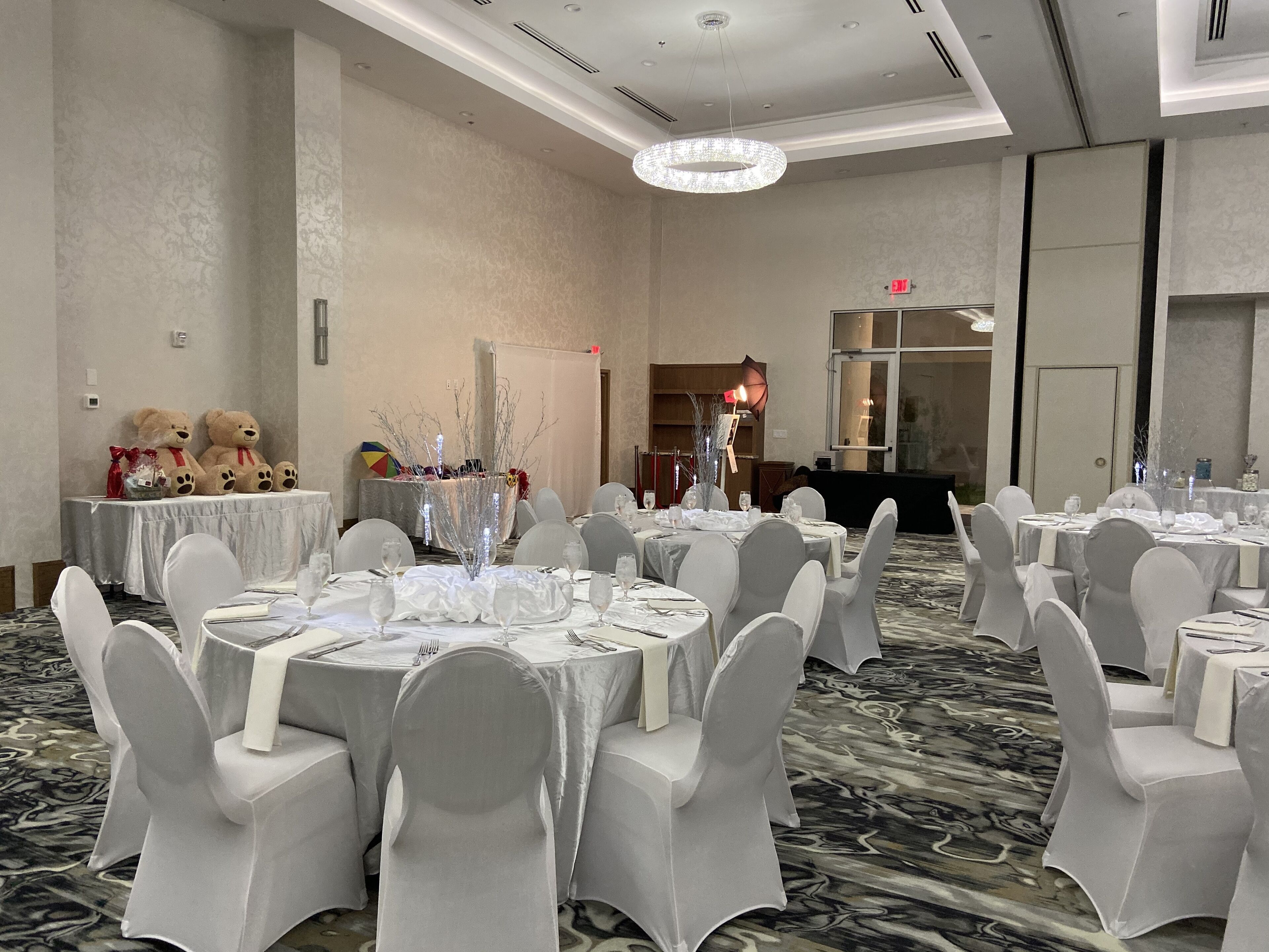 A banquet hall with round tables, white chairs, and a chandelier.