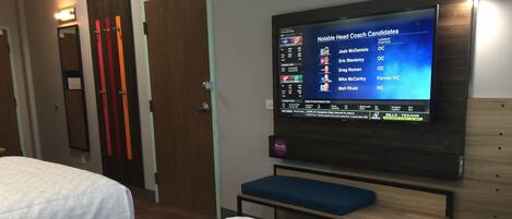 Habitación de hotel con dos camas, un televisor mostrando noticias deportivas y un banco.