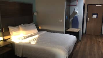 A hotel room with a bed, a nightstand, a desk, and a door.