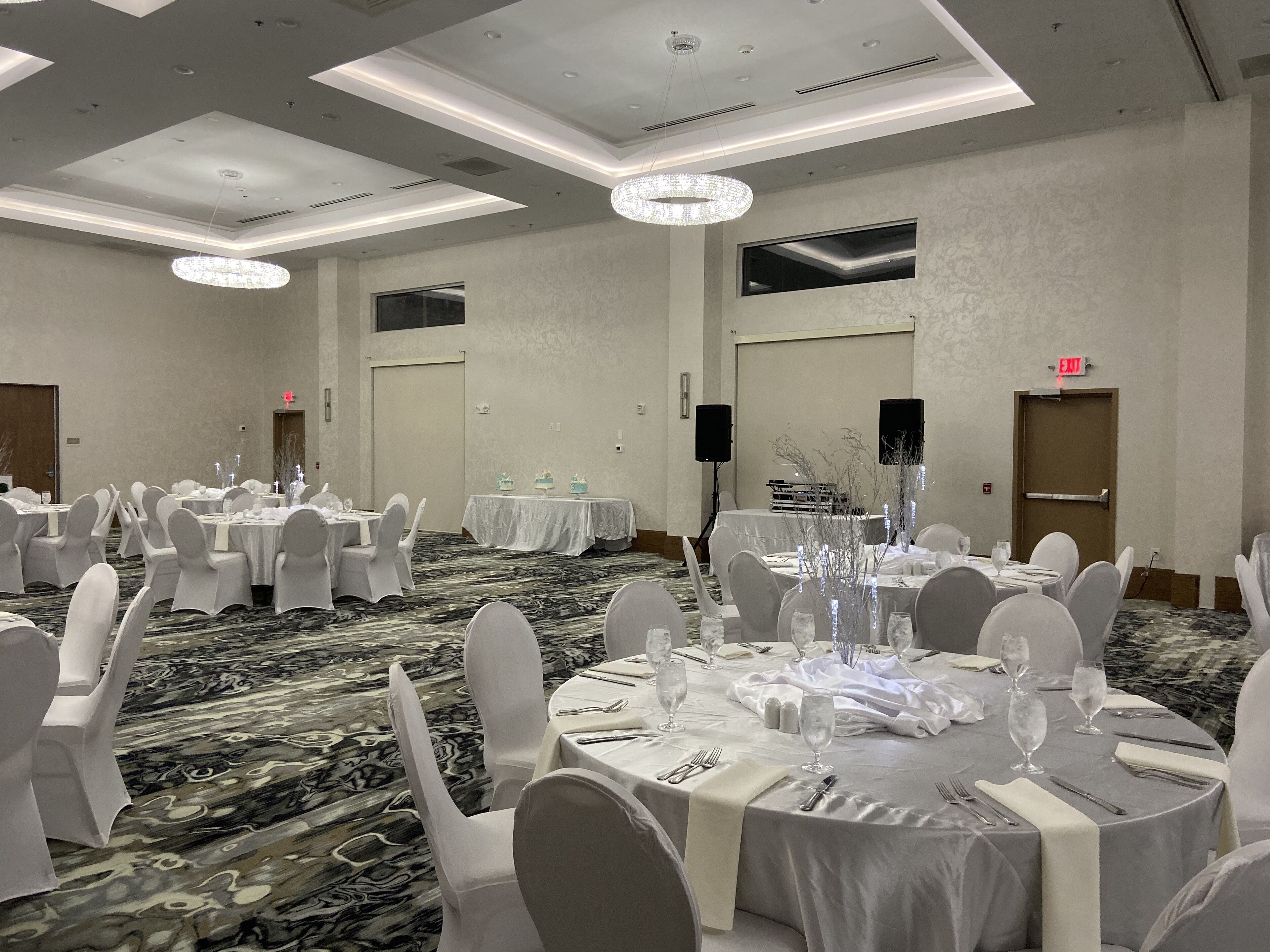 A banquet hall with round tables, white chairs, and chandeliers.