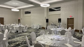 A banquet hall with round tables, white chairs, and chandeliers.