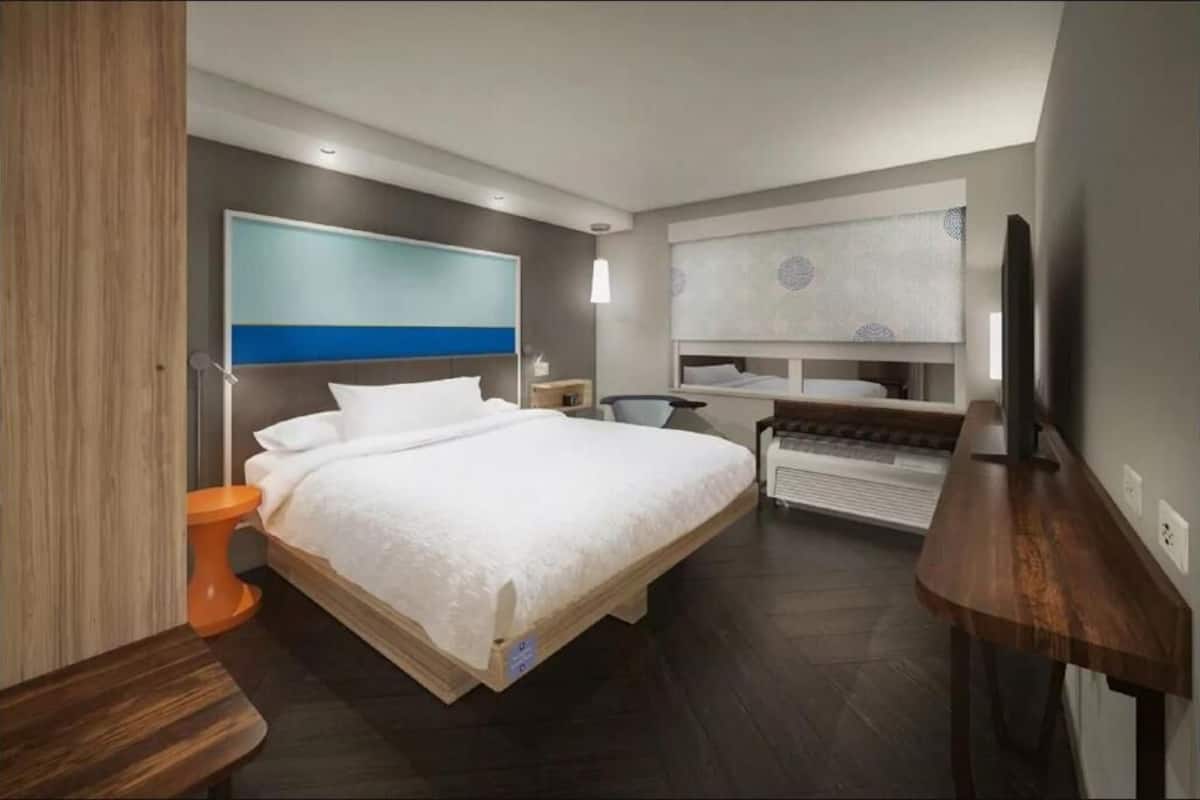 A modern hotel room with a large bed, a desk, a chair, and a television.