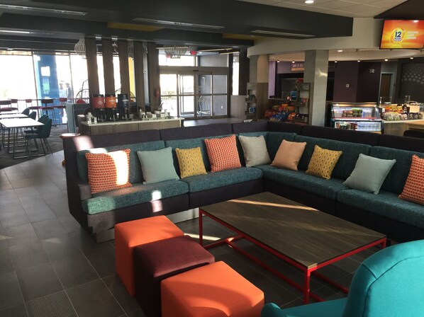 Un espace de détente moderne avec un grand canapé d’angle, des poufs orange et une table basse en bois.