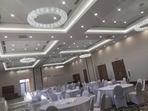 Une salle de banquet avec des tables rondes, des chaises blanches et des lustres.