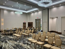 Un salón de conferencias con mesas y sillas redondas, una alfombra estampada y un candelabro.