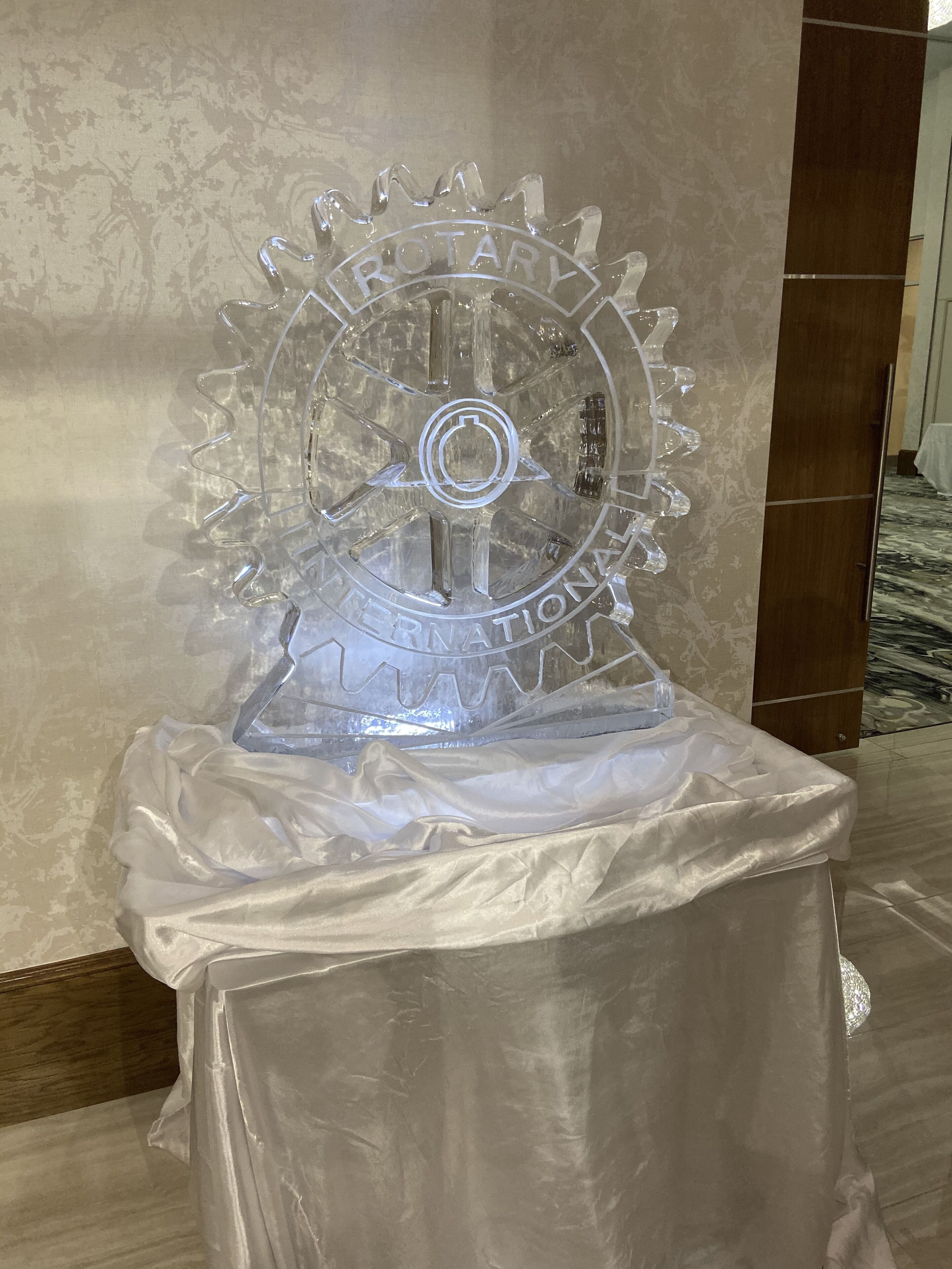 A clear glass sculpture with the inscription "ROTARY INTERNATIONAL" on a table covered with a white cloth.