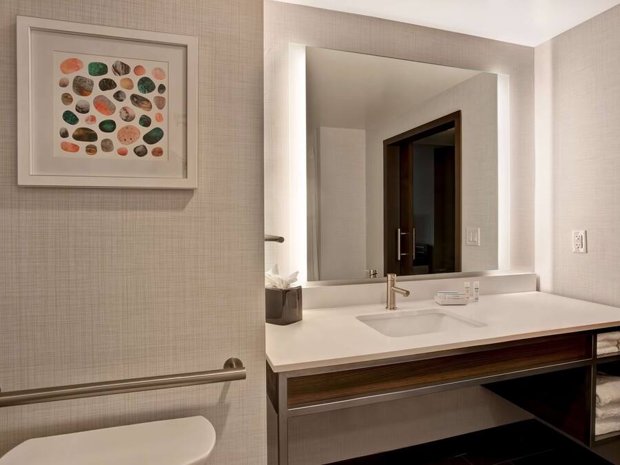 Un baño moderno con un lavamanos blanco, un espejo grande y una obra de arte enmarcada en la pared.