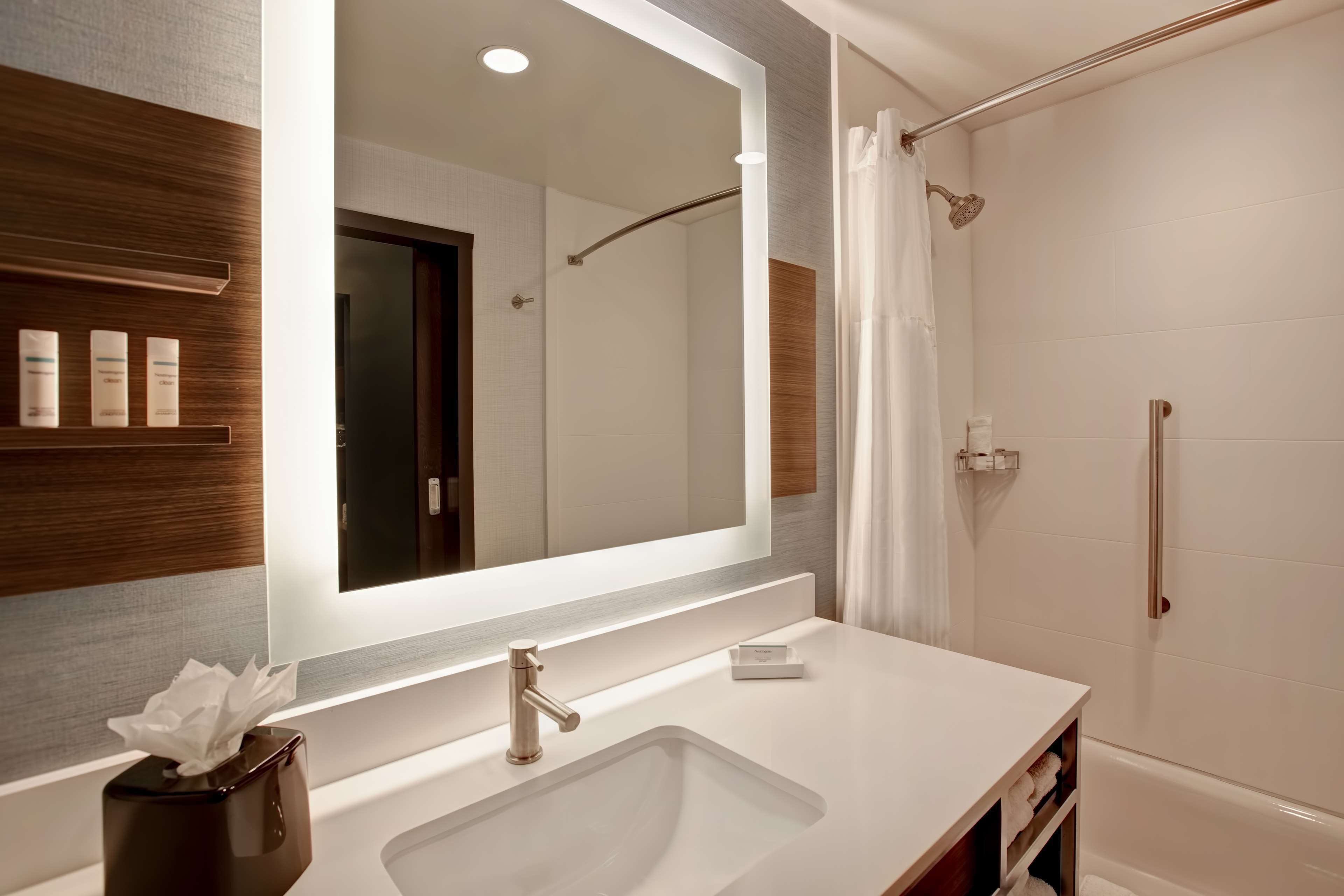 Un baño moderno con un espejo grande, un lavabo, una ducha y un perchero para toallas.